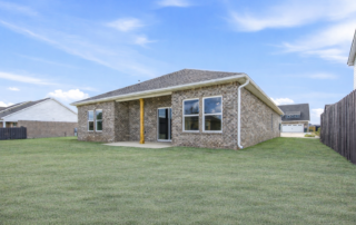 SpruceExteriorBack The Spruce floor plan by Maplewood Homes showing the backyard with covered patio, brick exterior, and spacious backyard with subtle spring greenery.